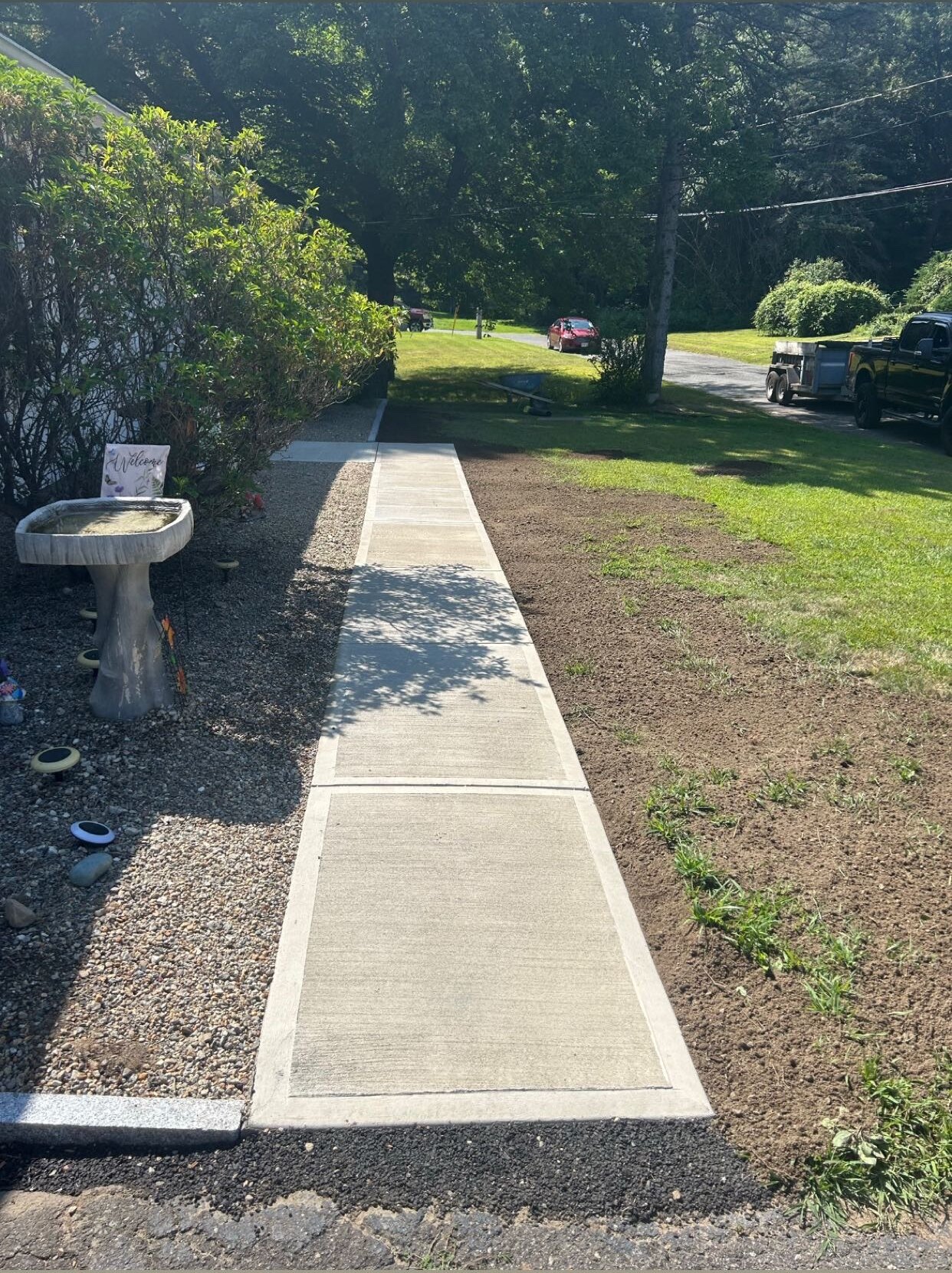 New straight concrete sidewalk with lawn restoration beside a home